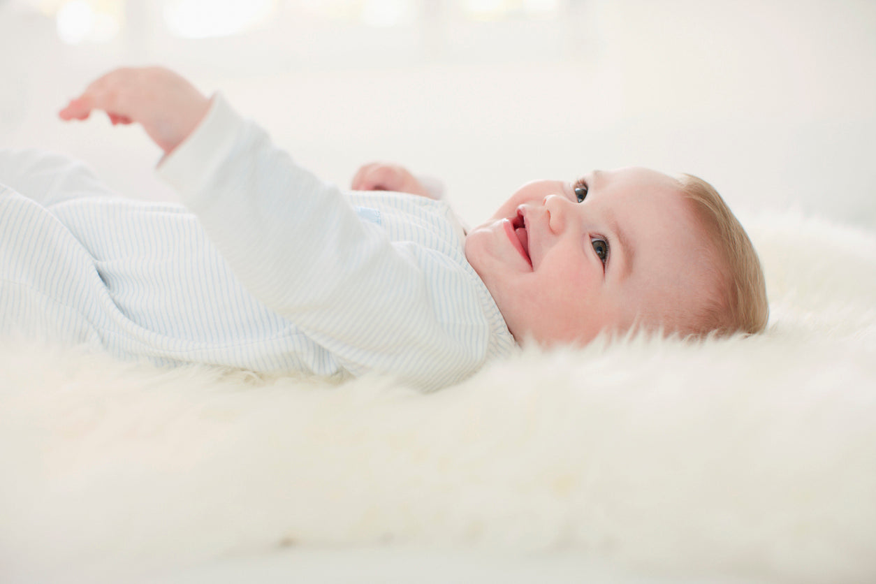 Fröhliches Baby liegt entspannt auf einem hellen Lammfell.